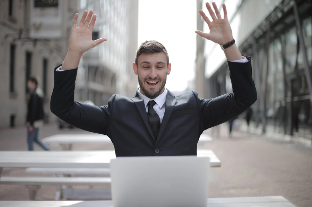 sistemas de gestão: imagem mostra um homem de terno e gravata com um notebook no colo com os braços para cima, comemorando